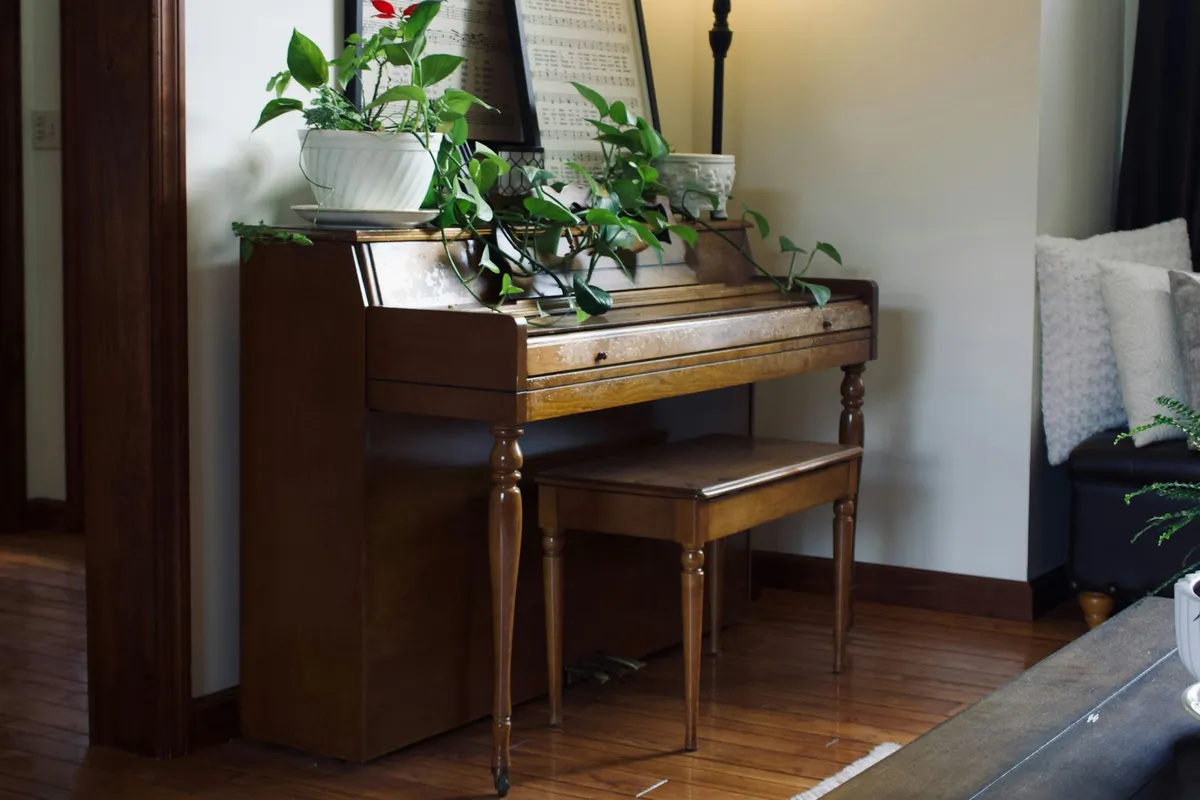 Wooden upright piano with a bench against a living room wall