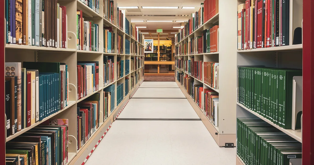 Long aisle of library shelving filled with books under overhead lights
