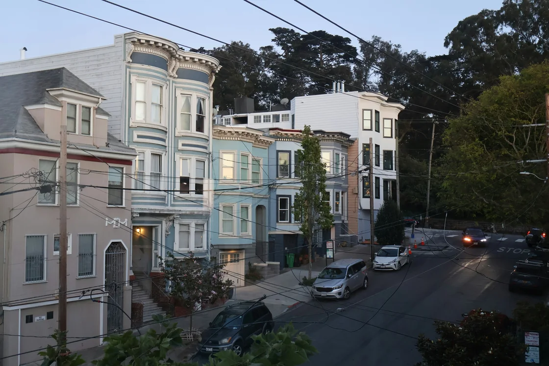 A San Francisco residential street lined with parked cars below Victorian homes